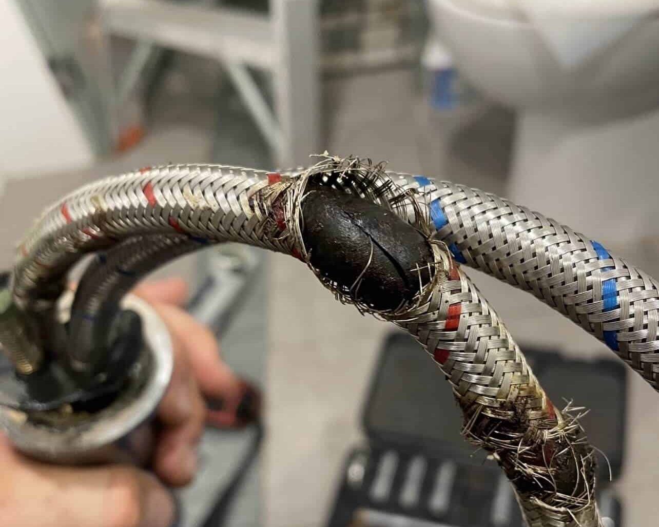 A burst braided flexi hose held up by a Goanna plumber, the rubber liner ballooning through the split braid