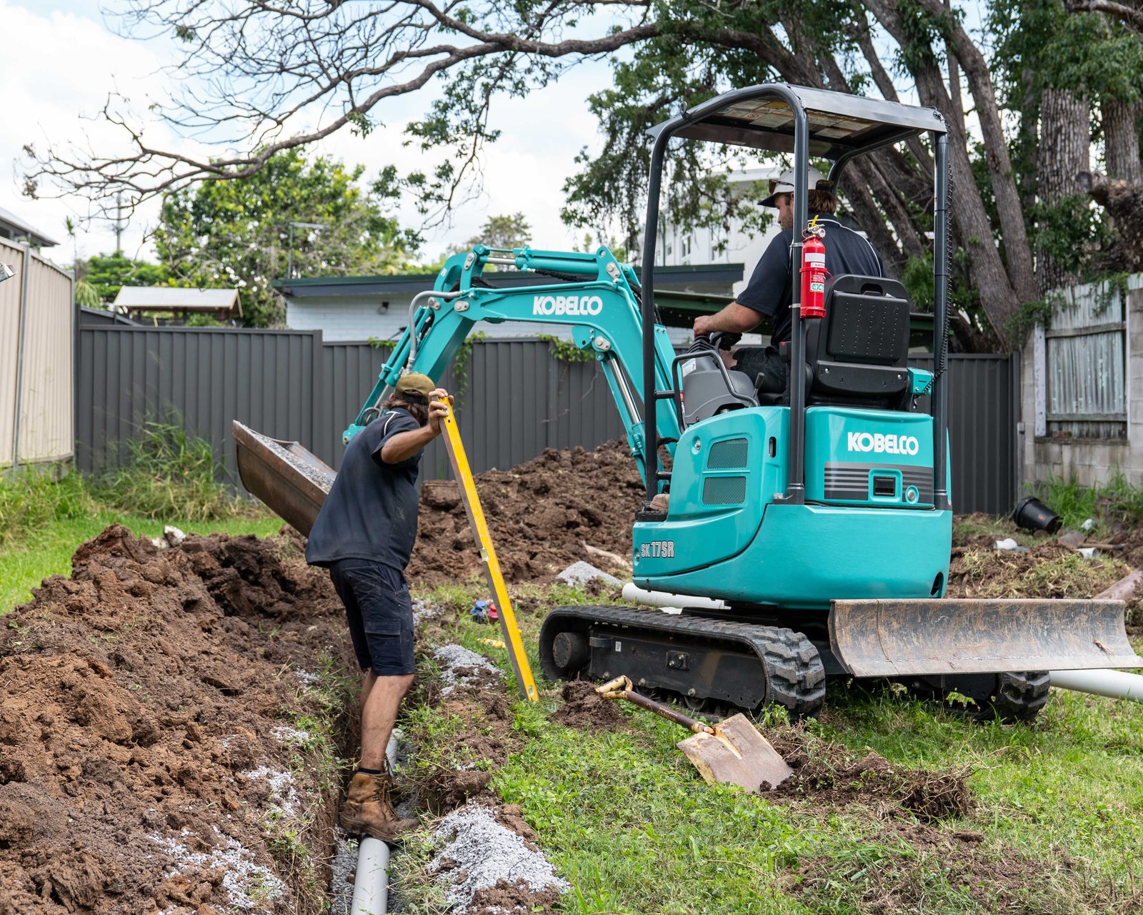 Goanna Plumbing mini excavator digging a drainage trench in a Brisbane backyard