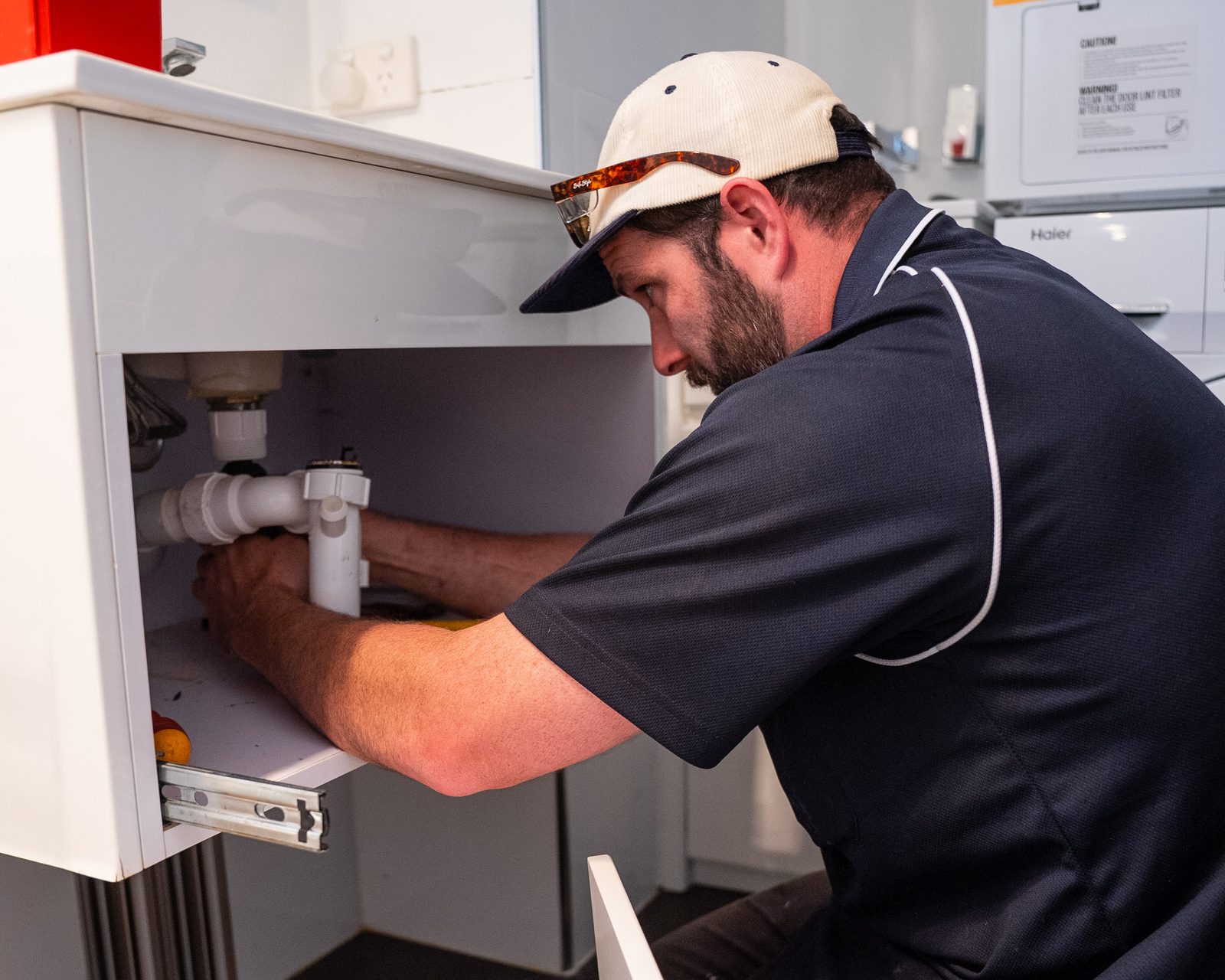 Jarred from Goanna Plumbing fitting a new waste trap under a kitchen sink