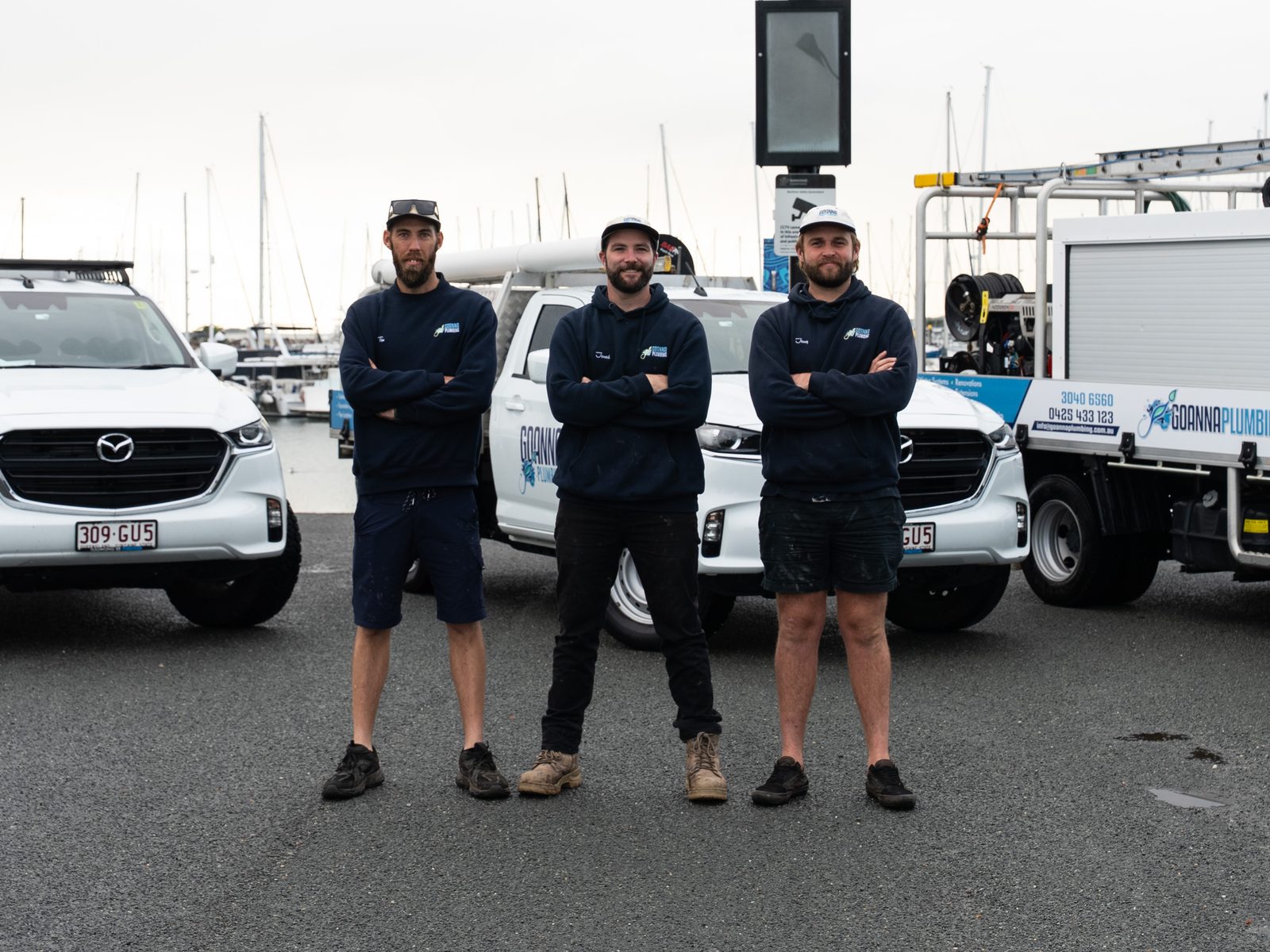 Jessy, Jarred and Tim from Goanna Plumbing standing with their vehicles at Manly Harbour