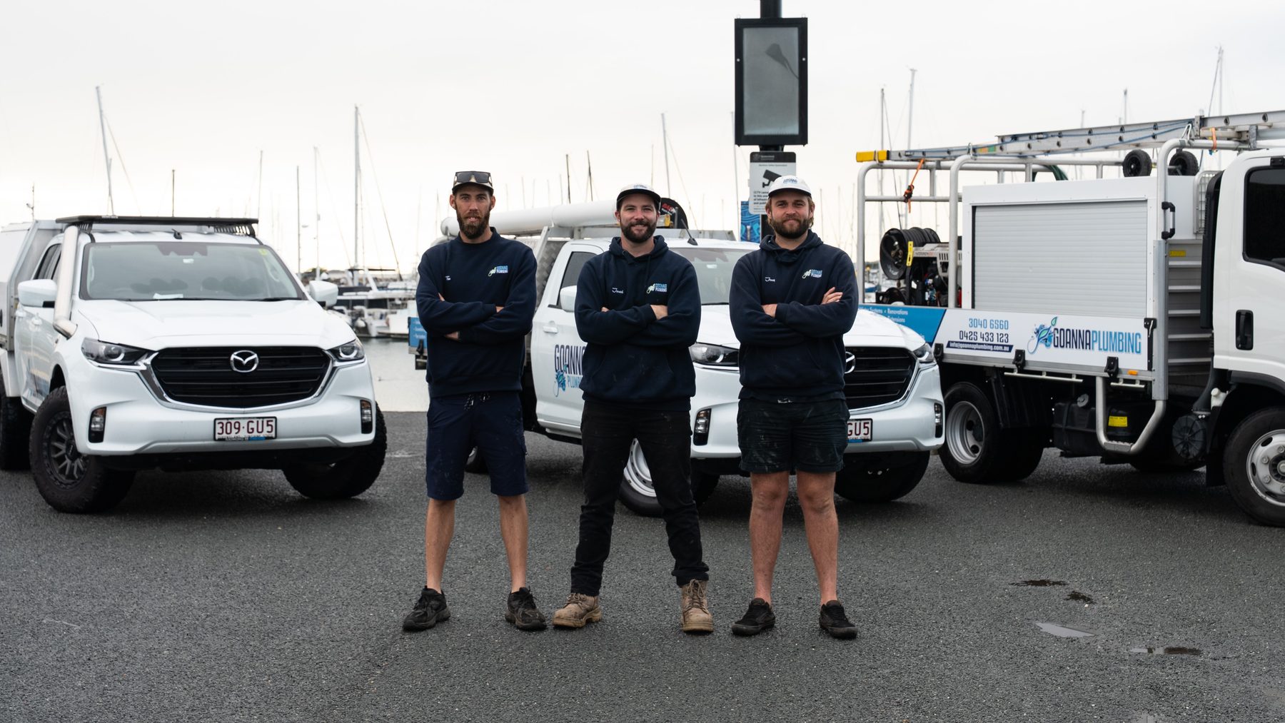 Jessy, Jarred and Tim from Goanna Plumbing standing with their utes and service truck at Manly Harbour